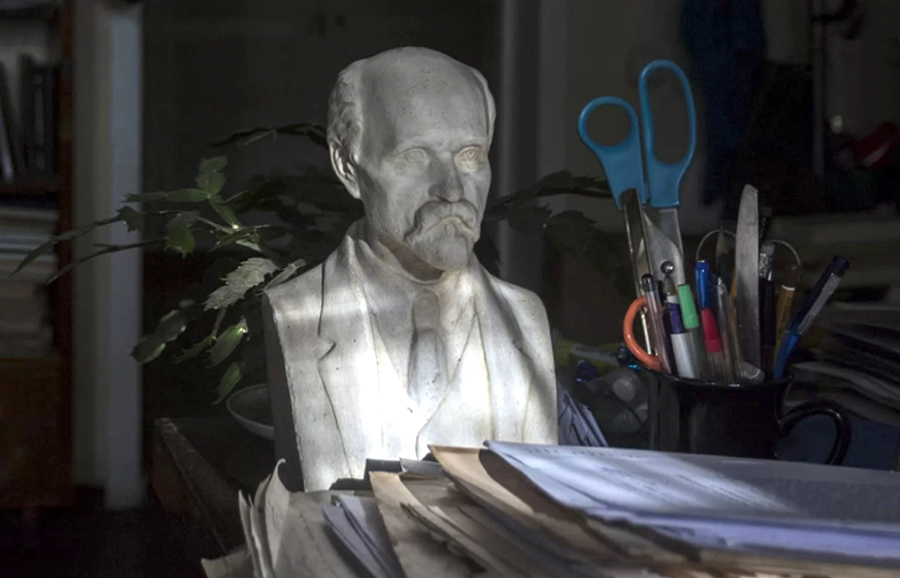Portreta skulptūra, kura atrodas uz darba galda starp papīriem, kancelejas rīkiem un grāmatām